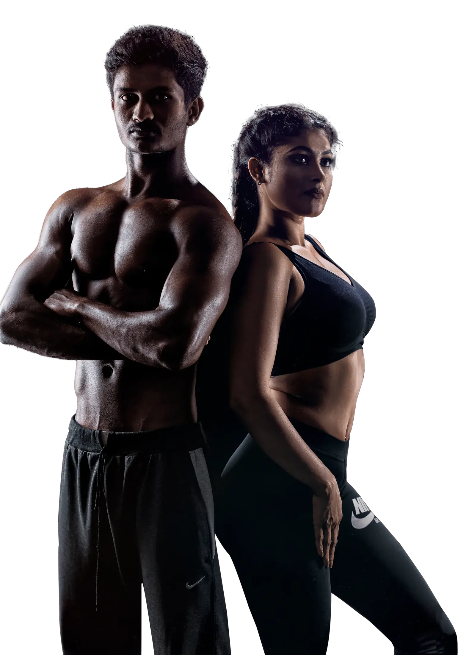 A man and a woman in black training wear stand back to back, arms folded, lit against a dark studio background