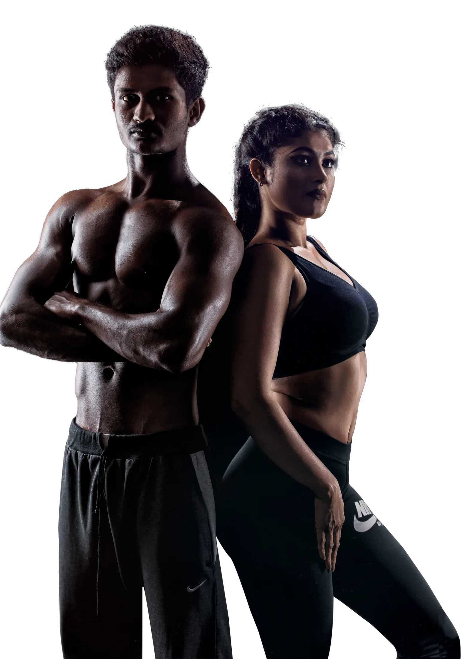 A man and a woman in black training wear stand back to back, arms folded, lit against a dark studio background